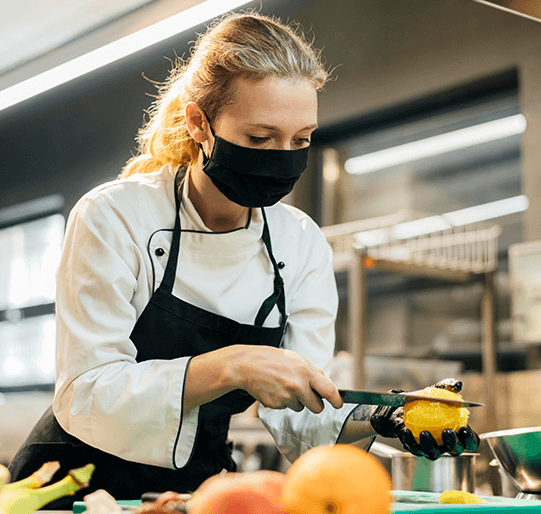 food-handler-certificate Woman wearing gloves and a mask while cutting a lemon.