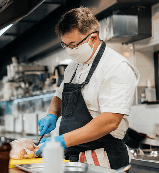 food-handler-certification Man wearing gloves and a mask while cutting a chicken.